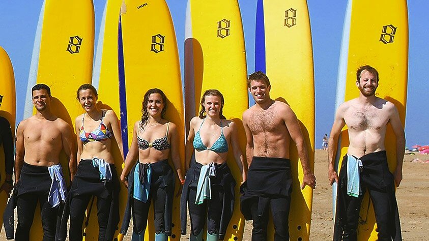 Groupe de débutants souriants apprenant à débuter le surf avec un moniteur à Anglet